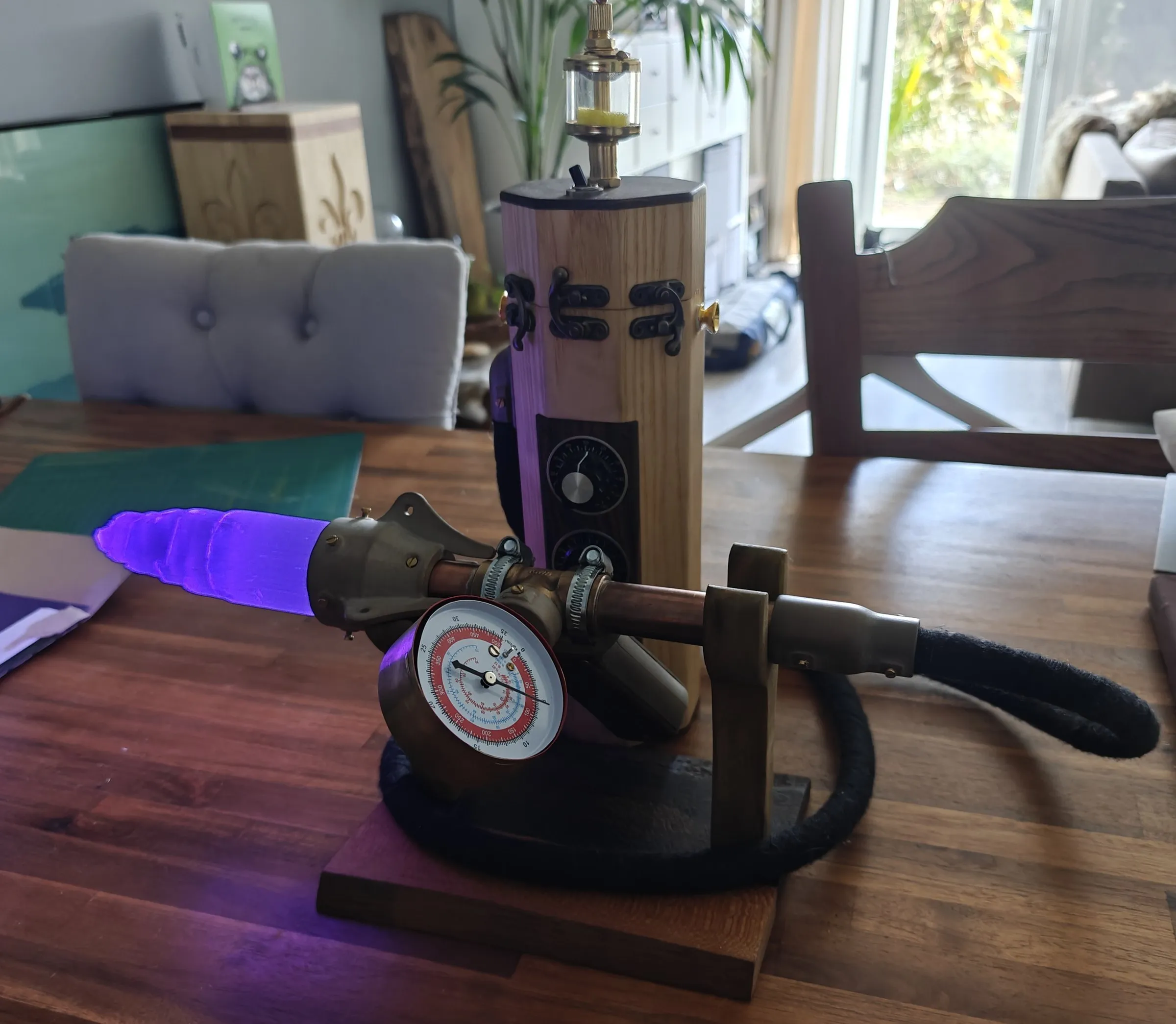 Ghost detector wand on its stand with the crystal glowing purple, a pressure gauge on top and a wooden canister behind it