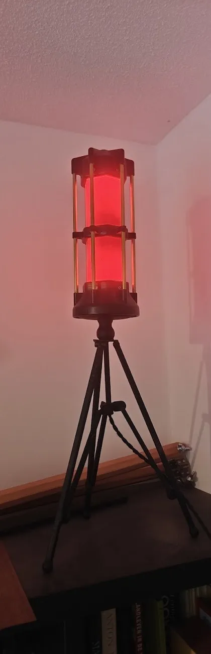 A shorter caged lantern glowing red on a tripod in the corner of a room