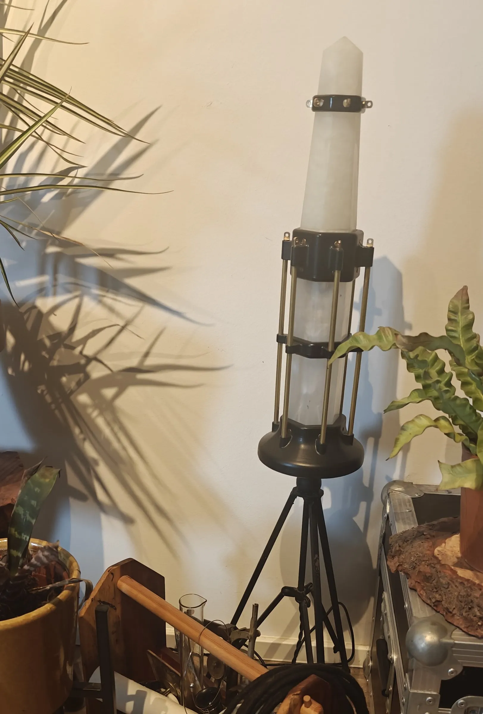 The tall lantern unlit on its tripod, with palm shadows on the wall