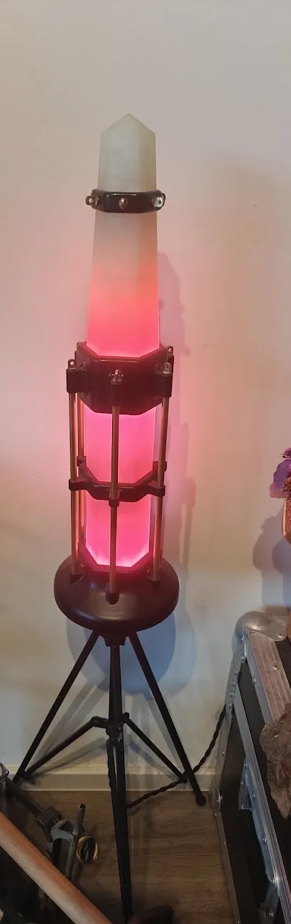 Tall lantern on a tripod glowing pink, with a pointed crystal on top of a caged column