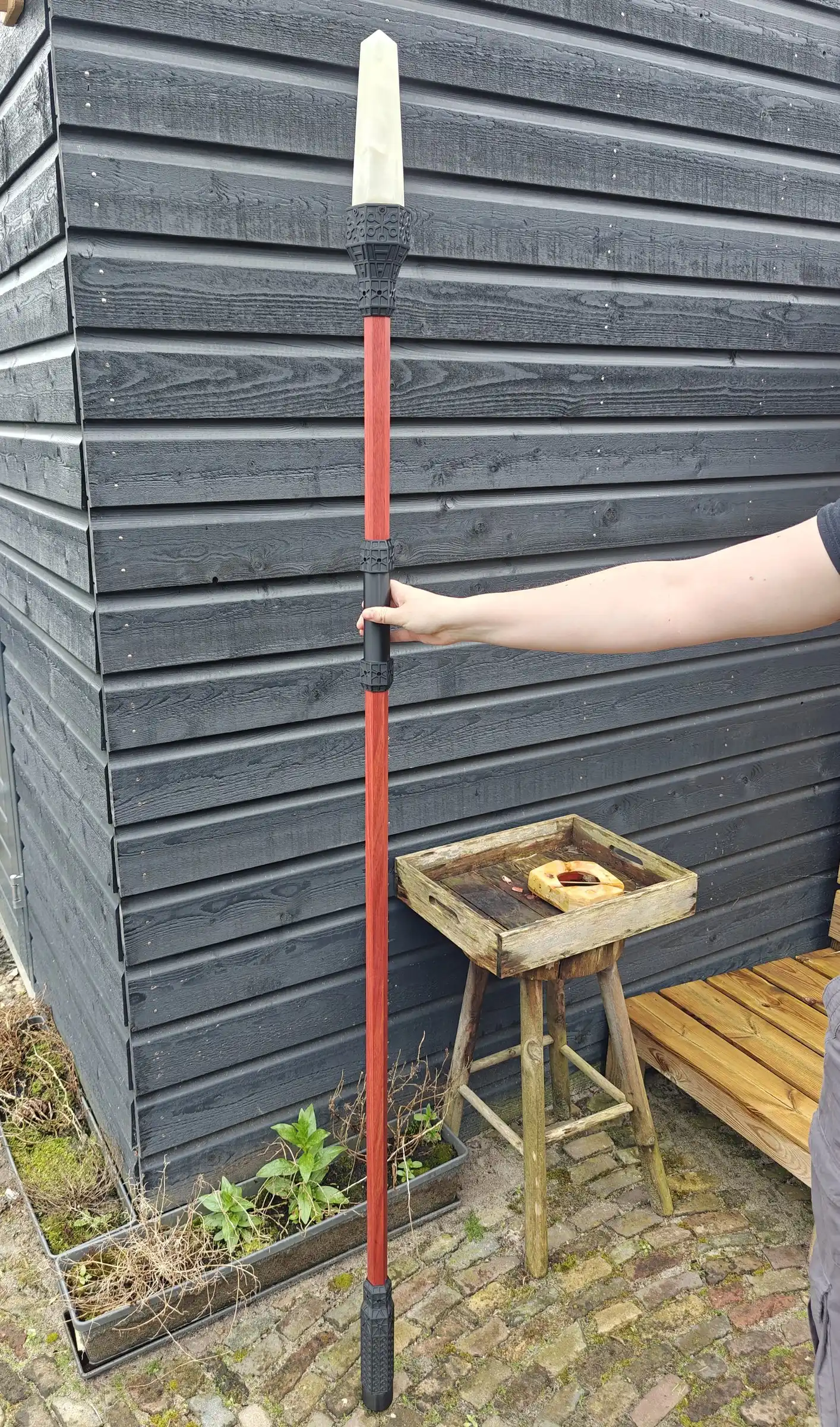 A complete Art Deco staff with a red wooden shaft, held upright at arm’s length
