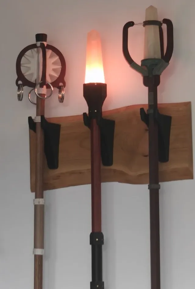 Three staves on a wooden wall mount, the middle one glowing warm orange in Torch mode